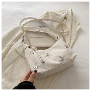 Détail du sac à bandoulière crème avec papillons argentés sur un blazer blanc pur