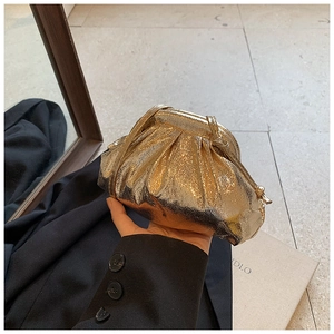 Close-up of golden metallic ruched shell bag held by hand with elegant pleated details