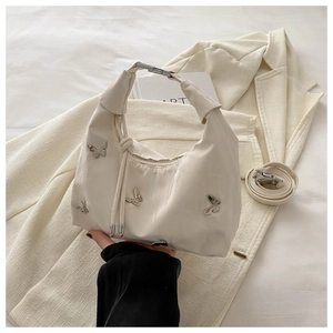 Détail du sac hobo blanc avec ornements papillons argentés et poignée à nœud élégante