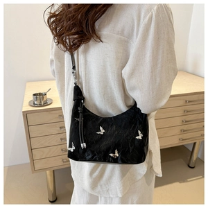 Detail of black pleated shoulder bag with silver butterfly charms worn by a model