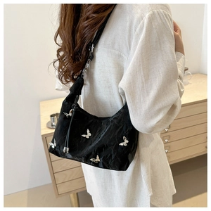 Détail du sac à bandoulière noir plissé avec breloques papillons argentées et sangle