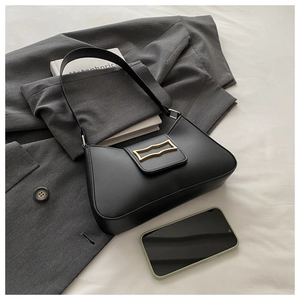 Détail du sac croissant noir avec boucle dorée géométrique sur fond de veste grise