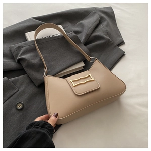 Détail du sac beige en forme de croissant avec boucle dorée sur une veste grise