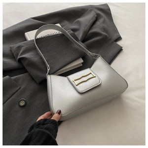 Sac à bandoulière argenté avec boucle dorée présenté sur une veste de blazer grise