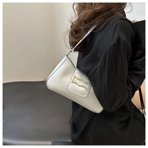 Gros plan d'un sac baguette argenté avec fermoir géométrique doré porté à l'épaule par un mannequin