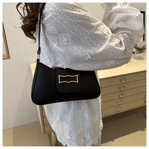 Détail du sac sous le bras noir mat avec boucle dorée sur un haut en dentelle