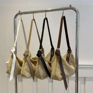 Woven straw tote bags in four colors with leather straps hanging on a metal rack