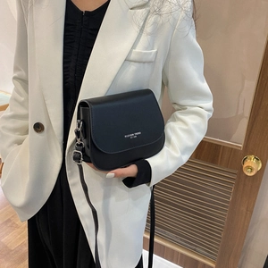 Minimalist black saddle crossbody bag with fashion trend typography worn over white blazer