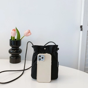 Minimalist black nylon drawstring crossbody bag shown next to a smartphone for size scale