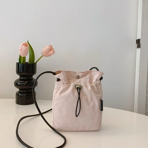 Minimalist light pink nylon crossbody drawstring bag with black fashion label on table