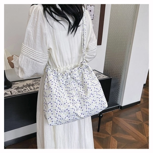 Close-up of a white tote bag with purple floral print and drawstring closure on a model