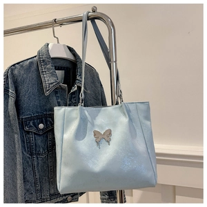 Détail du sac cabas bleu clair avec un ornement papillon en métal argenté et texture en cuir PU