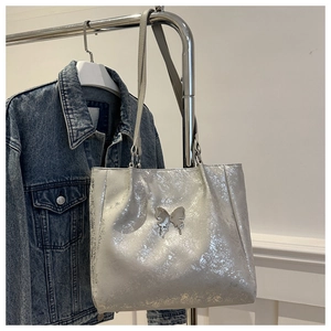 Détail du sac cabas argenté avec fermoir papillon métallique et texture sur jean bleu