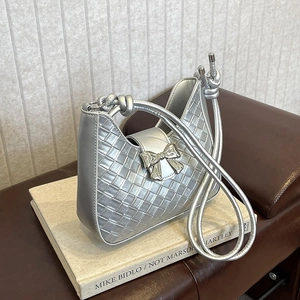 Silver woven underarm bag with a stylish bow decoration and knot handle on books