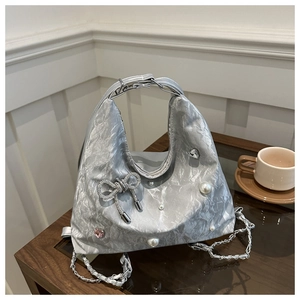 Detail of silver pleated handbag with rhinestone bow and pearl accents on wooden table