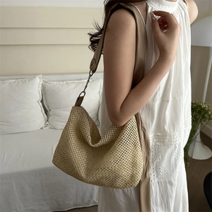 Bohemian woven straw tote bag with faux leather strap shown on shoulder in home setting