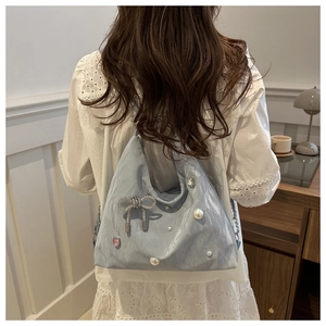Detail of light blue shoulder bag with pearl accents and rhinestone bow on a model