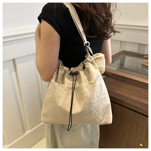 Dettaglio della grande borsa tote beige con coulisse, ciondolo in peluche e tracolla larga