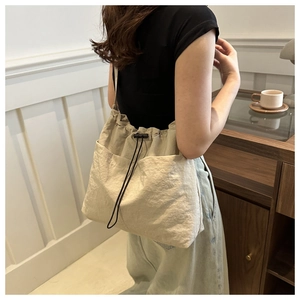 Detail of a minimalist drawstring shoulder bag in beige nylon featuring side pockets