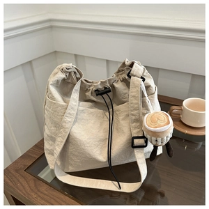 Detail of beige drawstring nylon bucket bag with wide strap and plush coffee cup charm