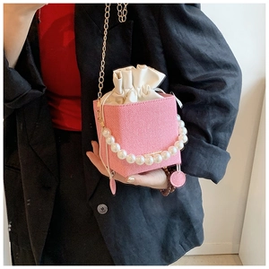 Pink cube bucket bag featuring pearl handle and gold chain detail in hand-held view