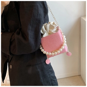 Close-up of pink bucket bag featuring woven texture, pearl handle, and gold chain strap