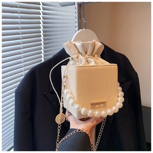 Detail of cream woven bucket bag featuring pearl handle and drawstring lining