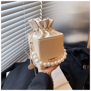 Detail of beige straw bucket bag with pearl handle and golden chain strap for women