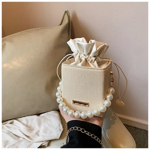 Detail of woven bucket bag with elegant pearl handle and cream leather drawstring closure