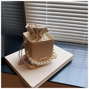Detail of woven bucket bag with elegant pearl handle and gold chain shoulder strap