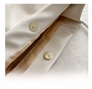 Close-up of golden magnetic snap button and interior zipper on beige tote bag