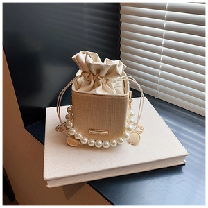 Detail of woven straw bucket bag with oversized pearl handle and gold chain strap
