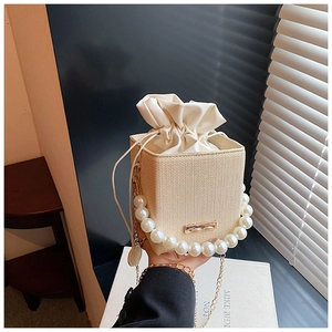Detail of straw woven bucket bag featuring large pearl handle and gold chain strap