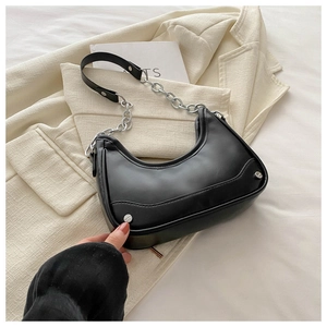 Detail of a black hobo bag with silver chain strap on a beige blazer background