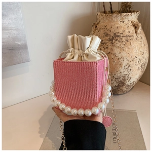 Detail of red and white knit bucket bag featuring a pearl handle and gold chain strap