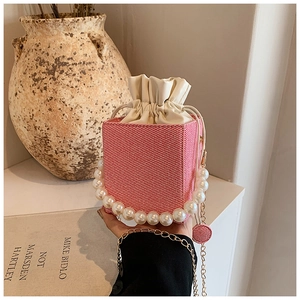 Pink woven mini bucket bag featuring a large pearl handle and golden chain strap detail