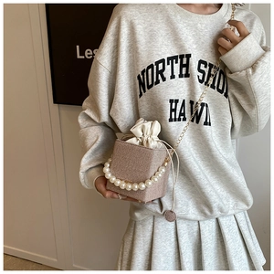 Close-up of woven bucket bag featuring pearl top handle and gold chain shoulder strap
