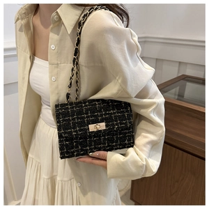 Detail of black tweed crossbody bag with gold chain strap and textured woven pattern