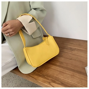 Close-up of bright yellow PU leather baguette bag held by model with smooth zipper detail