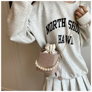 Detailed close-up of woven bucket bag featuring large pearls and gold chain strap