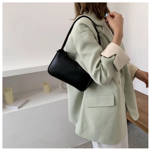 Minimalist black leather baguette bag worn by a model in a modern professional setting