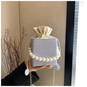 Detail of light blue bucket bag with woven texture, pearl handle and cream drawstring