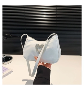 Close-up of white baguette bag featuring a sparkling rhinestone heart and metal zipper detail
