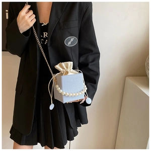 Detail of light blue textured bucket bag with pearl handle and golden chain strap