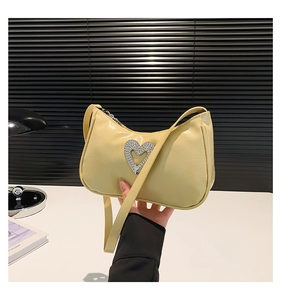 Detail of a cream faux leather handbag featuring a large sparkling rhinestone heart buckle