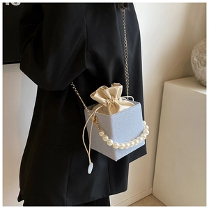 Detail of light blue textured bucket bag featuring pearl handle and gold chain strap