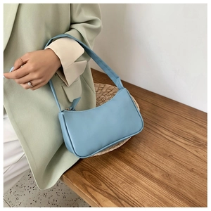 Side view of a sky blue leather hobo bag held by a model in a natural setting