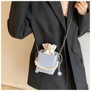 Detail of light blue crossbody bucket bag with pearl handle and golden chain strap