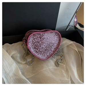 Pink heart-shaped sequin crossbody bag with silver chain strap on white silk background