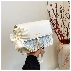 Detail of elegant woven crossbody bag with cream satin bow and gold logo flap